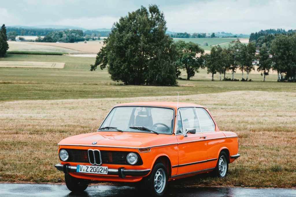 BMW Oldtimer in Orange vor Wiese mit Bäumen